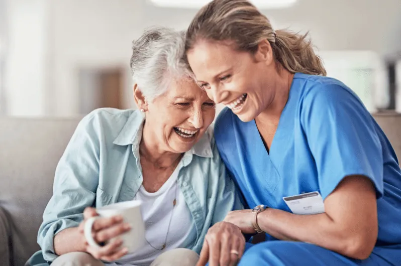 Caregiver and senior woman laughing together over coffee