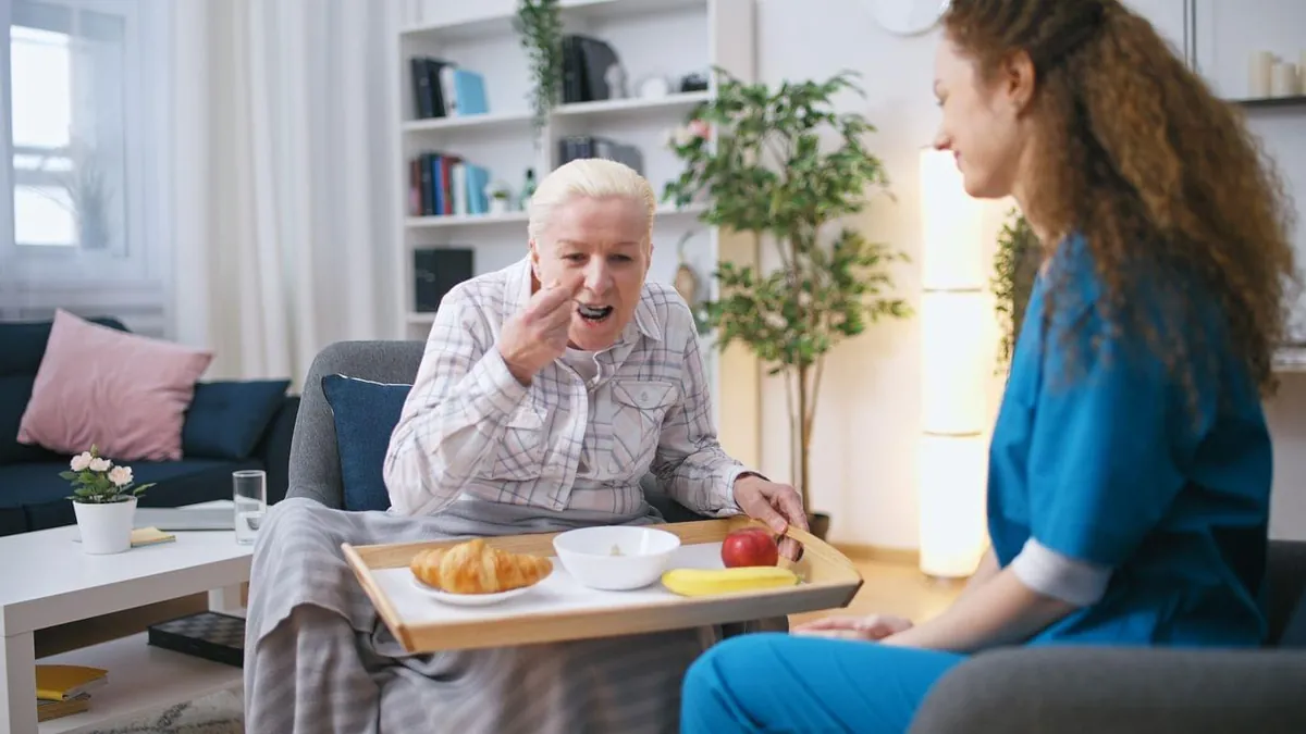 Caregiver bringing a breakfast tray to a senior woman in a chair