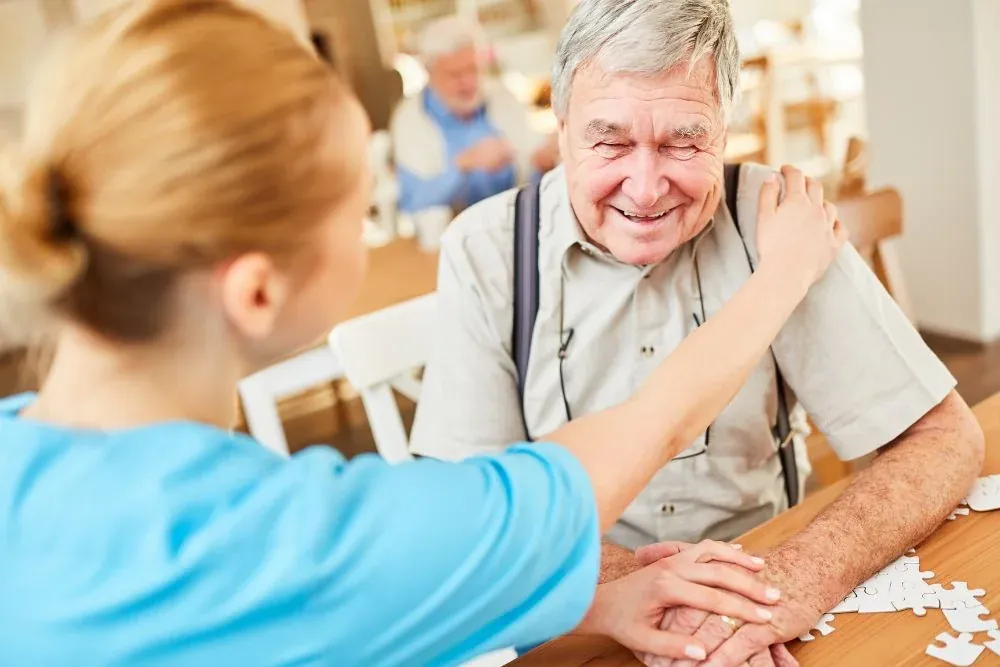 Caregiver resting a hand on a smiling senior man's shoulder