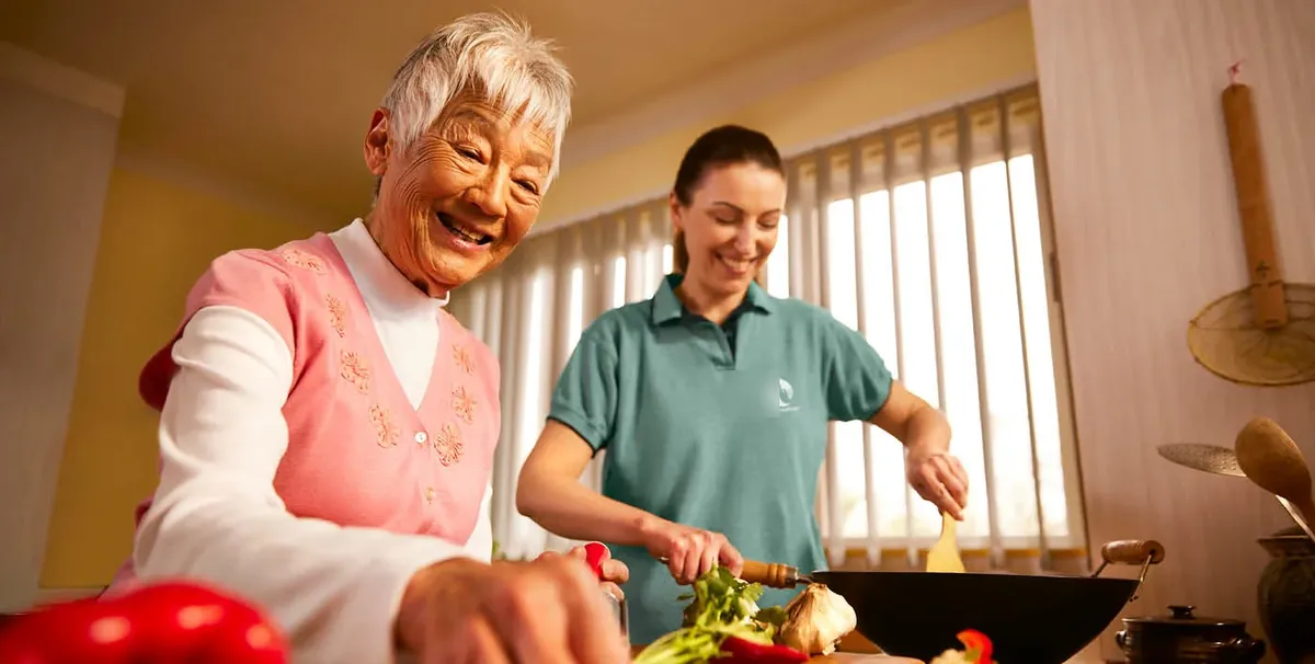 Caregiver cooking in the kitchen with a smiling senior woman