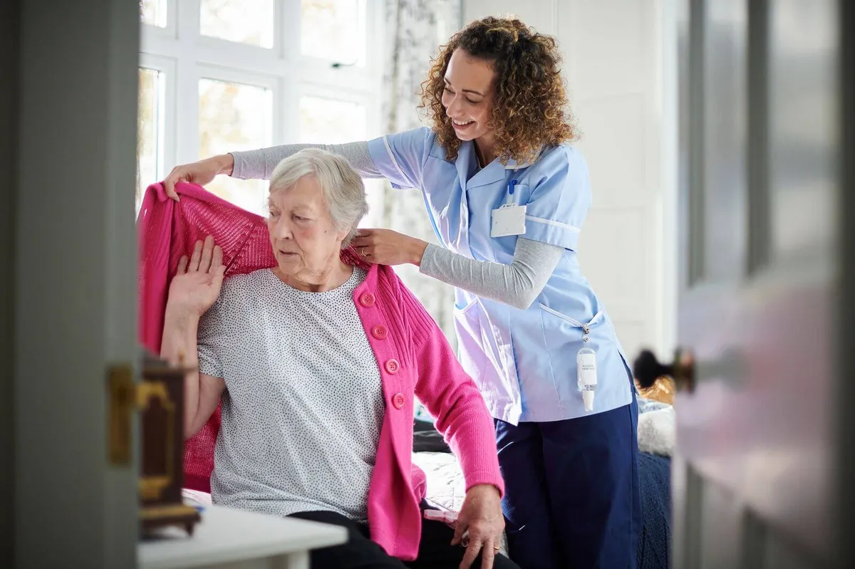 Caregiver helping a senior woman put on a cardigan