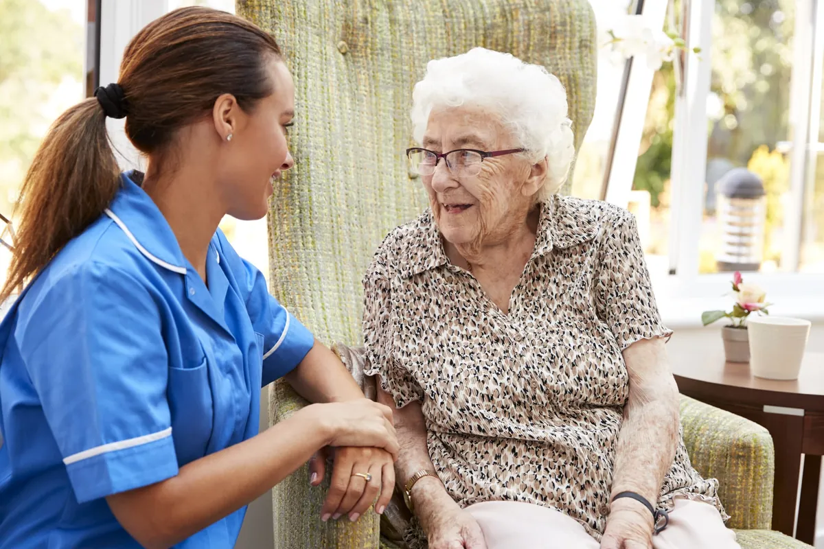 Caregiver holding a senior woman's hand in a bright living room
