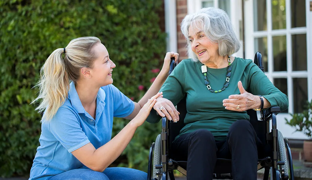 Caregiver kneeling to talk with a senior woman in a wheelchair