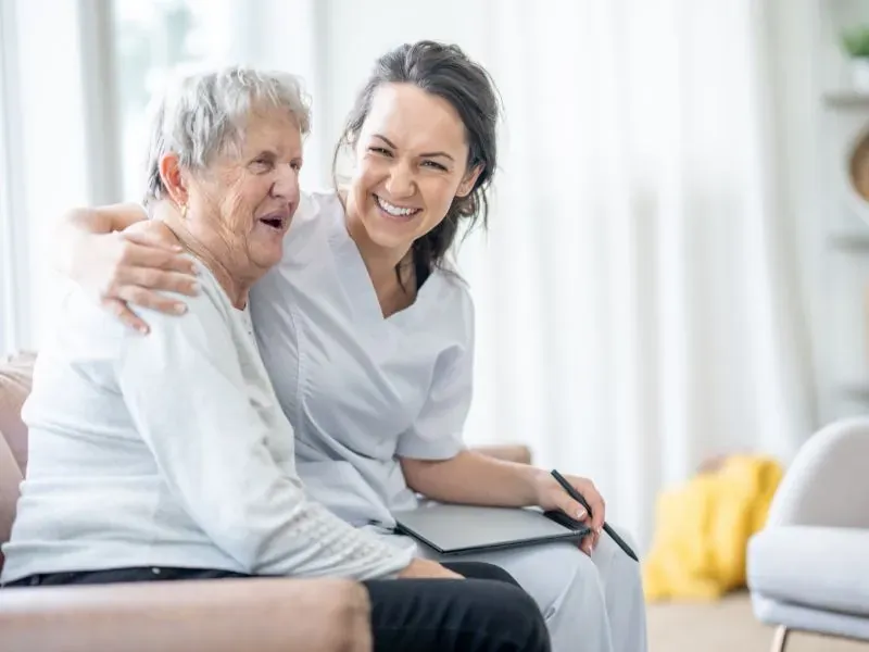 Caregiver laughing with a senior woman on a couch at home