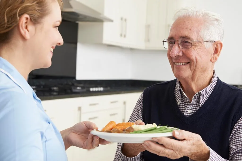 Caregiver handing a plate of home cooked food to a senior man