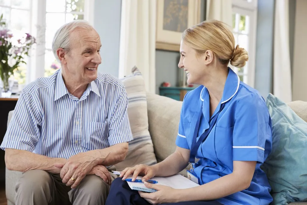 Caregiver taking notes while talking with a senior man on a sofa