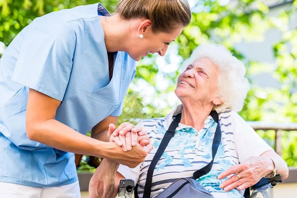 Caregiver smiling with a senior woman in a wheelchair outdoors