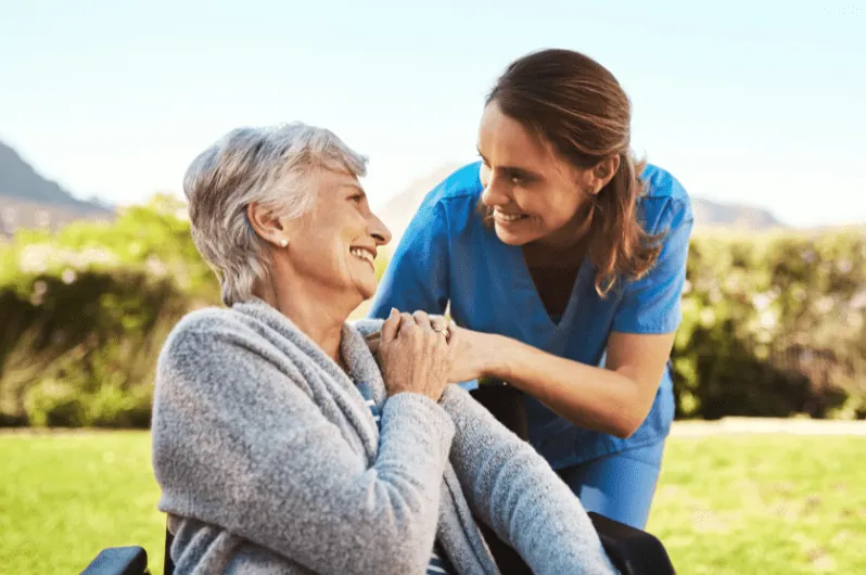 Caregiver pushing a senior woman's wheelchair through a park