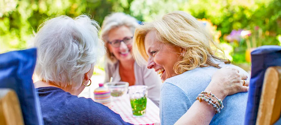 Three older friends laughing together around a garden table